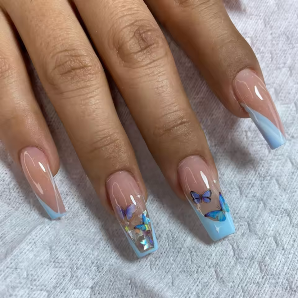Trendy coffin nails with a nude base, blue tips, and delicate butterfly designs, showcasing a chic and whimsical nail art style for 2025.