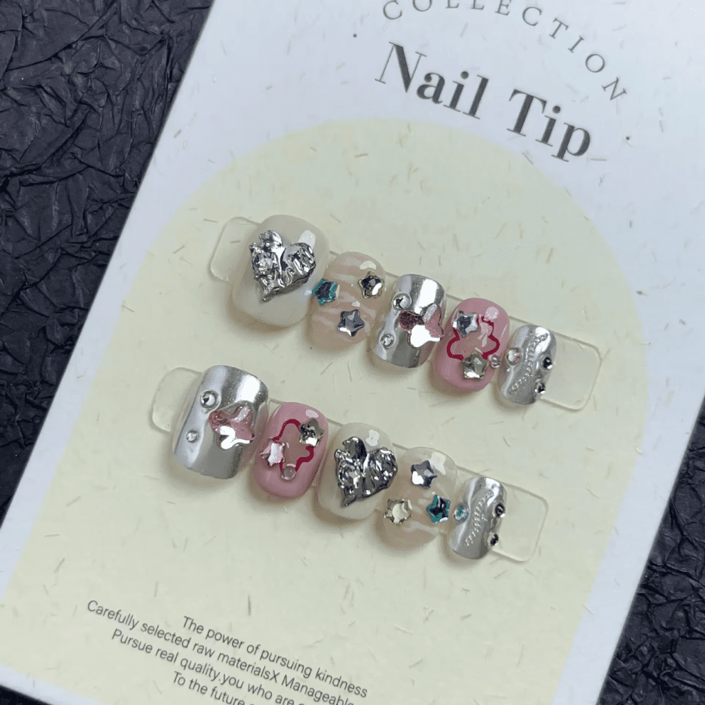 A set of nail tips with metallic silver, pink, and white bases, adorned with 3D embellishments like hearts, stars, and rhinestones, arranged on a card that reads "COLLECTION Nail Tip".