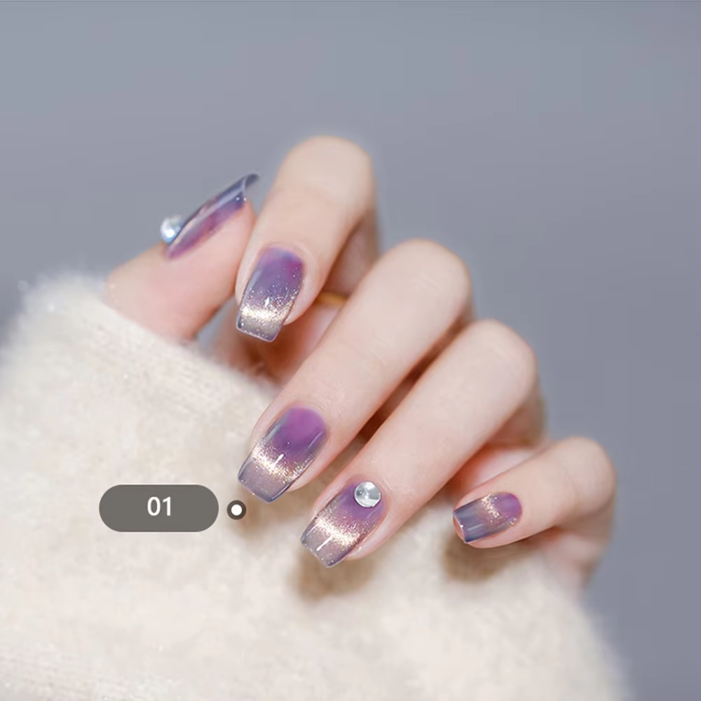 A close-up of a hand with gradient purple and silver nail art, featuring a small gem on one nail.