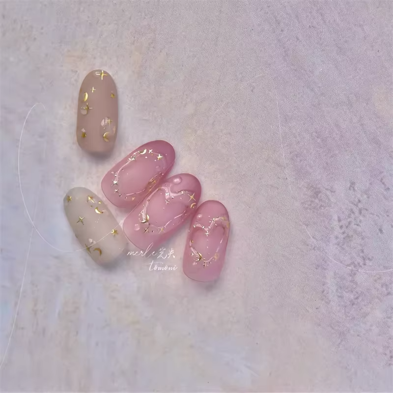 Set of translucent pink and beige artificial nails decorated with small gold stars and abstract lines, arranged in a semi-circle.