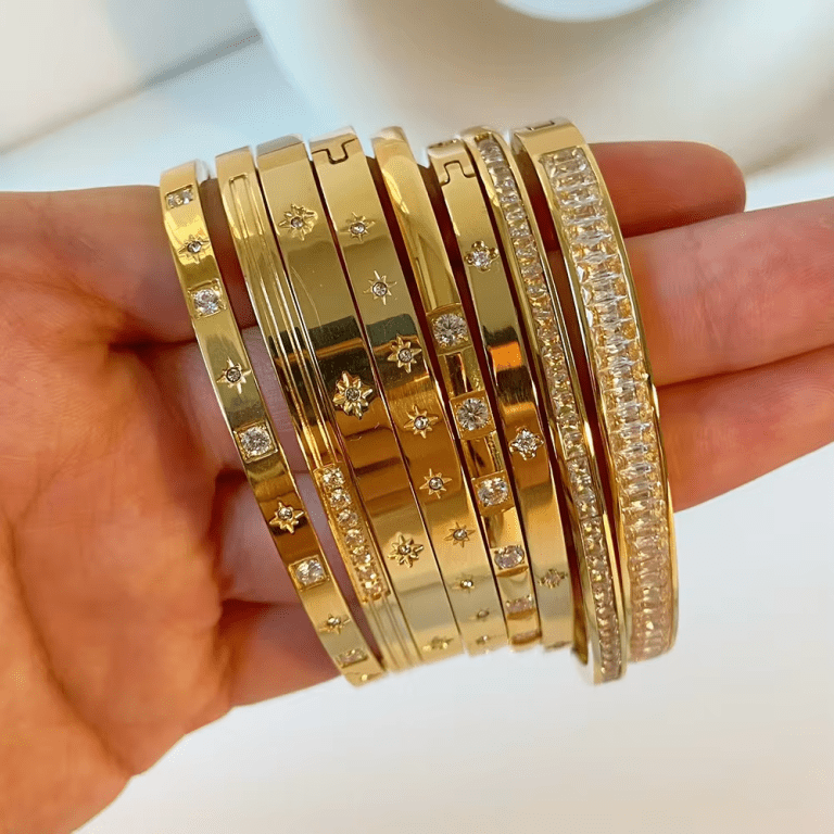 A hand holding multiple gold-colored bangles adorned with cubic zirconia stones.